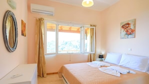 A bedroom with a bed, a bedside table, a lamp, a window with curtains, and a painting on the wall. - Eros Sea View in Kentroma (Corfu)