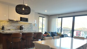 A modern kitchen with a marble countertop, a central island with bar stools, a dining area with a large table and chairs, and a balcony with a view of buildings. - New! Slick designer apARTtment with bay views. (Cabo San Lucas)