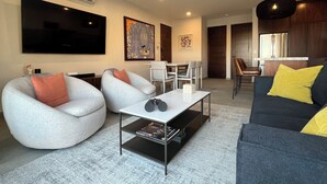 A modern living room with a flat-screen TV, comfortable seating, a coffee table, and a kitchen area in the background. - New! Slick designer apARTtment with bay views. (Cabo San Lucas)