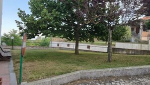 A courtyard with a grassy area, a stone wall, and a building with a tiled roof.