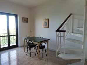 Une pièce comprenant une table à manger et des chaises, un escalier et de grandes fenêtres.