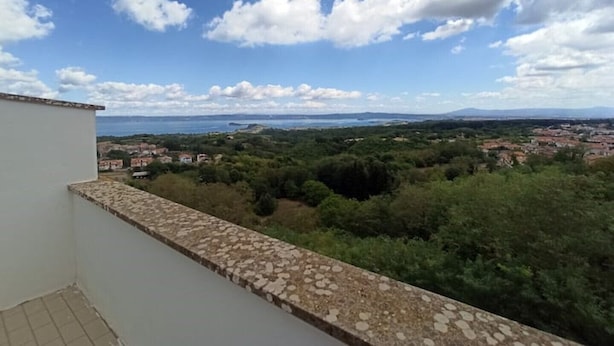 A balcony with a stone balustrade overlooking a coastal landscape with buildings and greenery.
