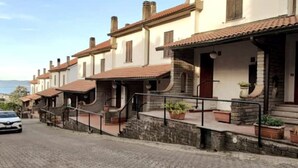 A row of traditional buildings with stone steps and tiled roofs, a paved street, and a car parked on the side.