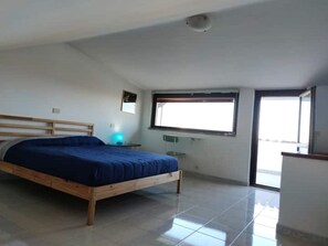 Une chambre à coucher avec un lit en bois, une petite table de chevet, une fenêtre et une porte donnant sur un balcon.