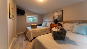 Une chambre avec deux lits, une fenêtre, un téléviseur à écran plat et un tableau au mur.