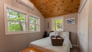 A bedroom with a wooden ceiling, two windows, a bed with pillows, a bedside table, a bench, and a wall-mounted air conditioner. - The Hideaway, lake views & access sleeps 8 Now featuring AC Wi-FI and TV (Alton)