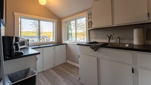 A modern kitchen with white cabinets, a black countertop, a sink, and a coffee maker. - Delightful Lake View Cabin in Alton Bay Now featuring Lake Access, AC/ TV/ WiFi (Alton)