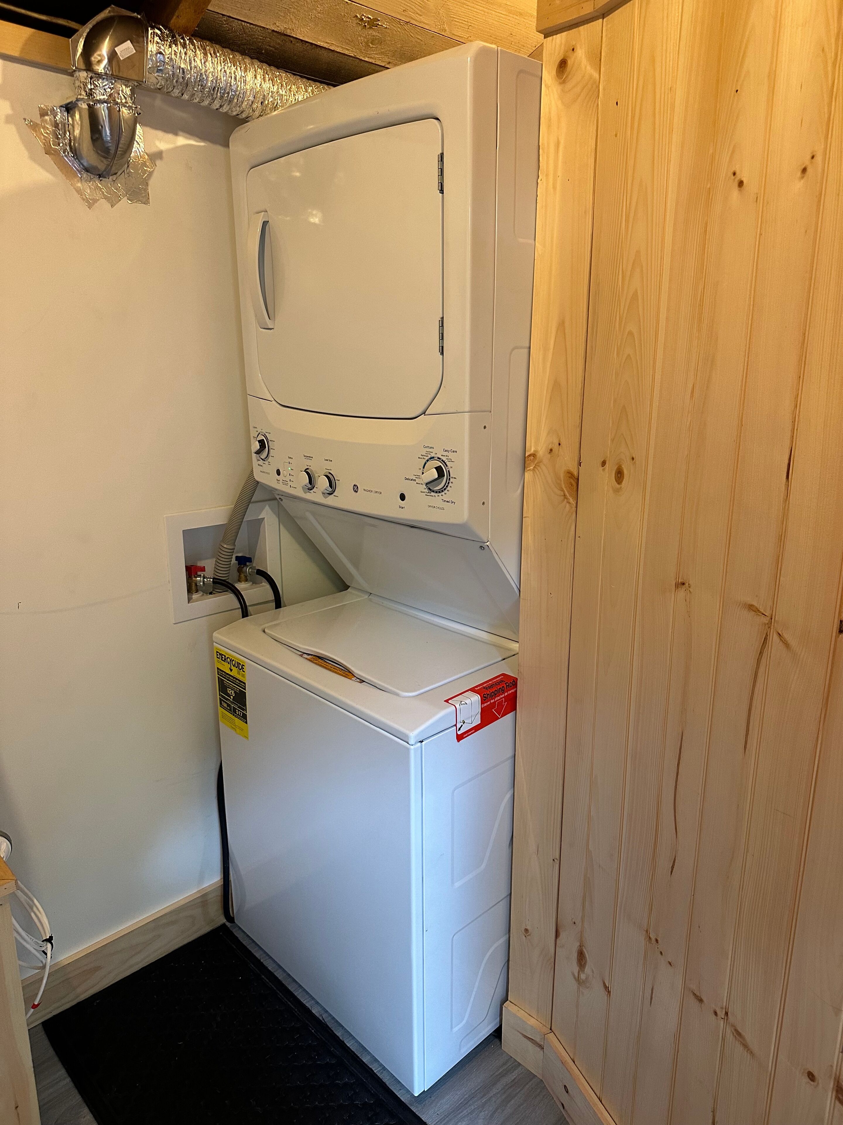 Ein kleinerer Waschraum mit einer Frontlader-Waschmaschine und einem Trockner, einer sichtbaren Steckdose und einer Holzvertäfelung.