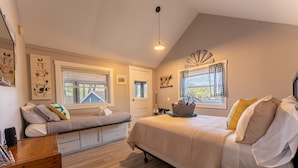 Un dormitorio acogedor con una cama grande, un banco con almohadones, una mesita de noche y una ventana con cortinas.