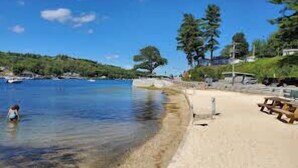 A beach with clear water, a sandy shore, and a few trees in the background. - Lake View Cabin in Alton Bay Now featuring Lake Access, AC/ TV/ WiFi (Alton)