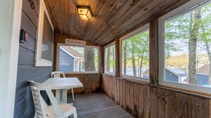 A covered porch with a table and chairs, wooden walls, and large windows. - Lake View Cabin in Alton Bay Now featuring Lake Access, AC/ TV/ WiFi (Alton)