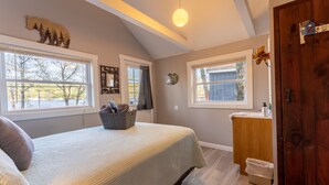 A bedroom with a bed, windows, a wooden door, a small bathroom, and a ceiling light. - Cabin for two with lake views & access Now featuring AC Wi-FI and TV (Alton)