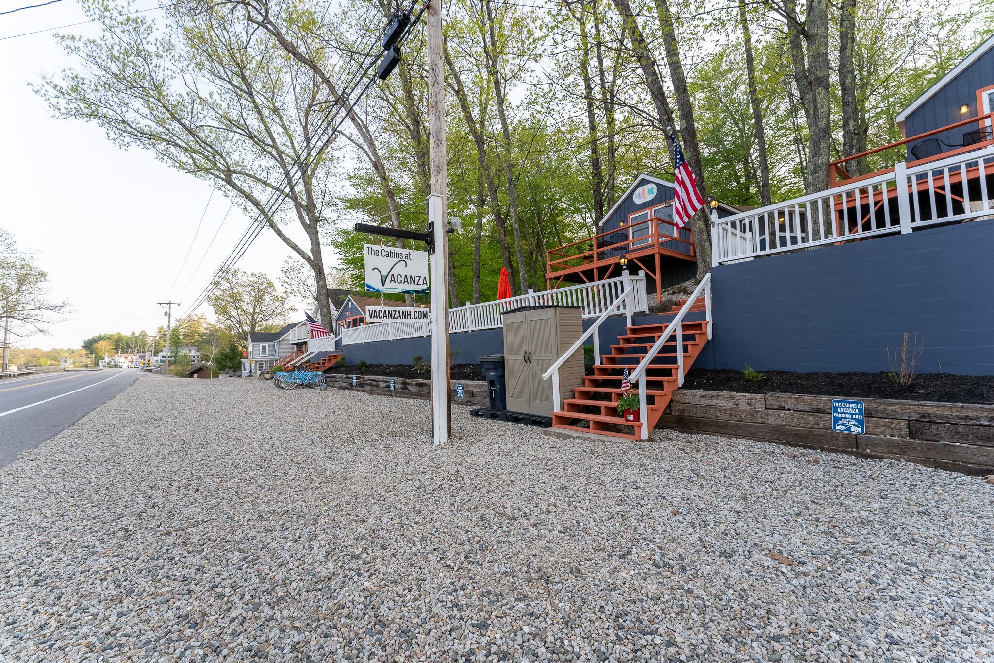 A cabin-style building with a staircase leading to a deck, surrounded by trees and a gravel path.
