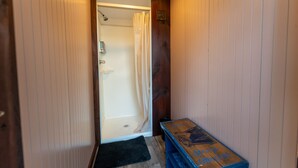 Un couloir étroit aux murs lambrissés, un espace douche séparé par un rideau et un petit banc avec une pancarte.