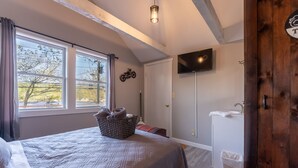 Une chambre à coucher avec un lit, un téléviseur fixé au mur, une fenêtre avec des rideaux et une porte en bois.