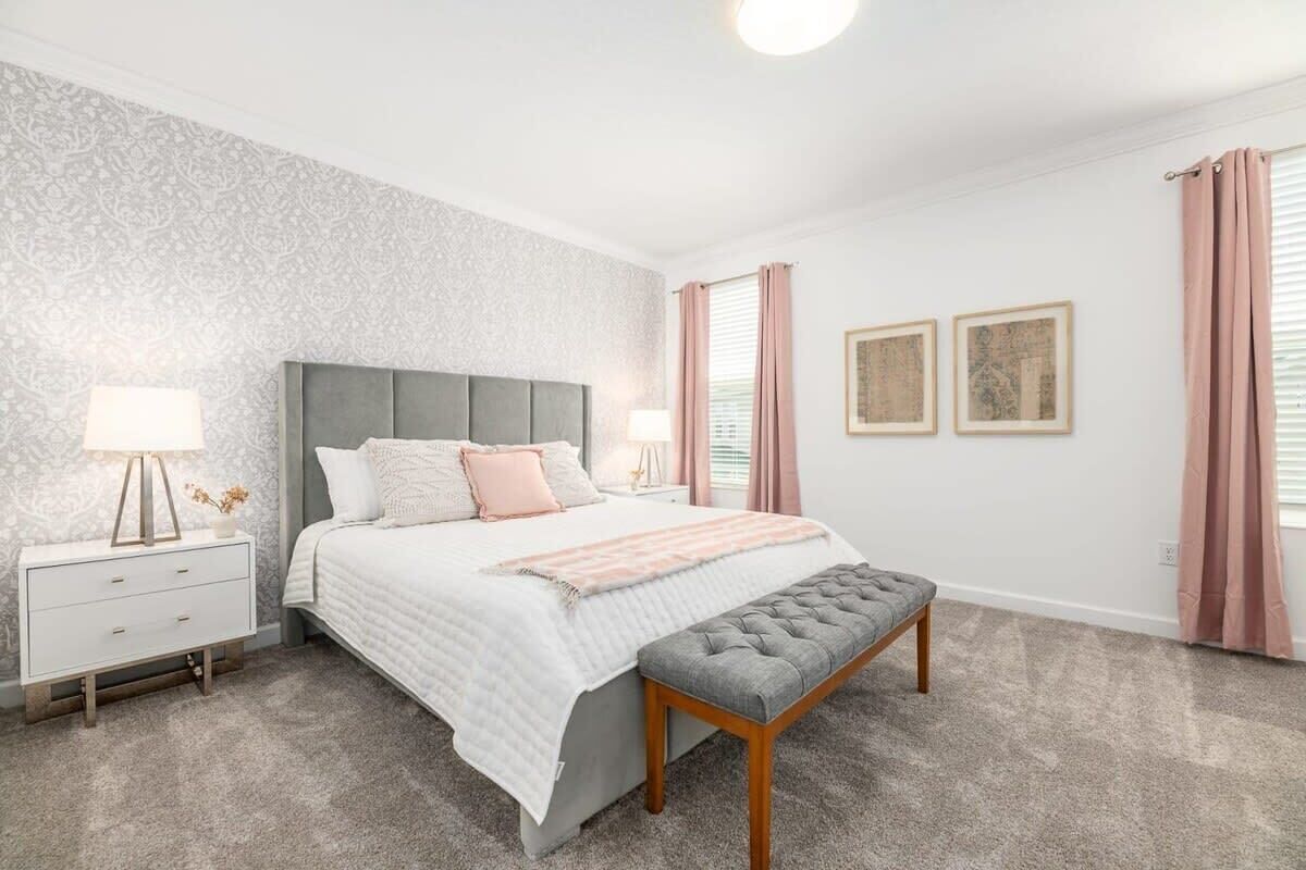 Un dormitorio con cama, mesita de noche, lámpara y un banco.