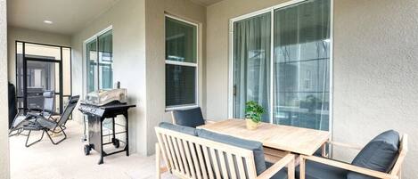 A balcony with a wooden table and chairs, a grill, and a potted plant.