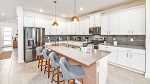 A modern kitchen with white cabinets, stainless steel appliances, and a central island with bar stools. - Super luxury home, private pool, premium location (Kissimmee)