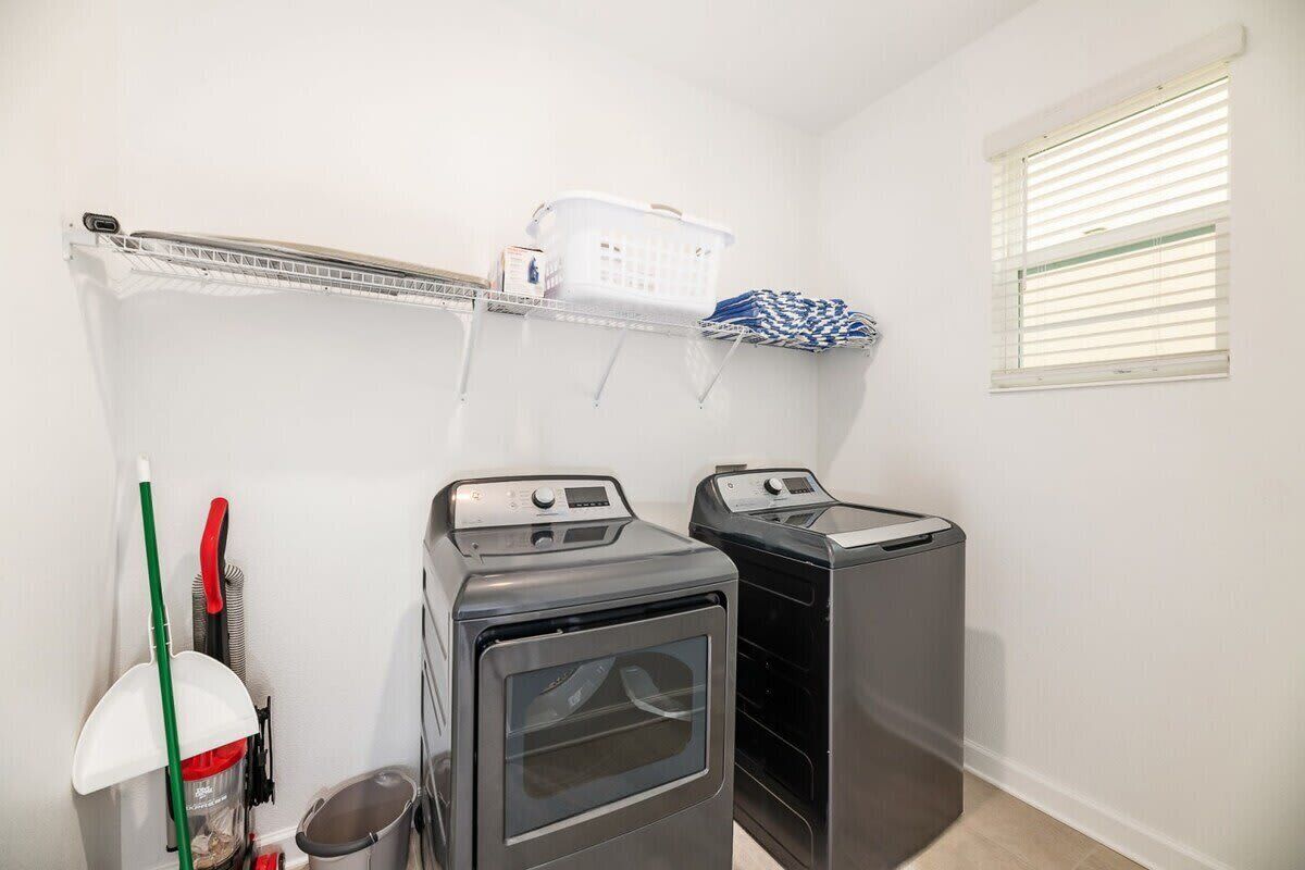 A laundry room with two front-loading washing machines, a drying rack, and a window with blinds.