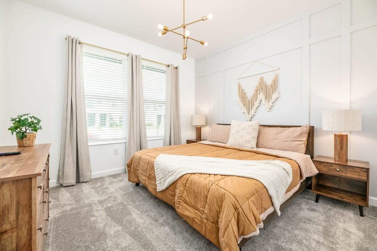 Une chambre avec un grand lit, une commode en bois, une plante et un luminaire fixé au mur.