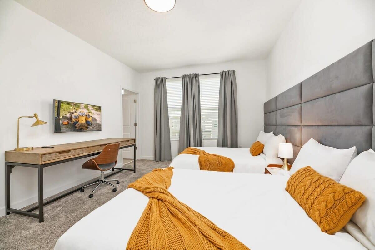 Een hotelkamer met twee bedden, een bureau, een stoel, een lamp en een schilderij aan de muur.