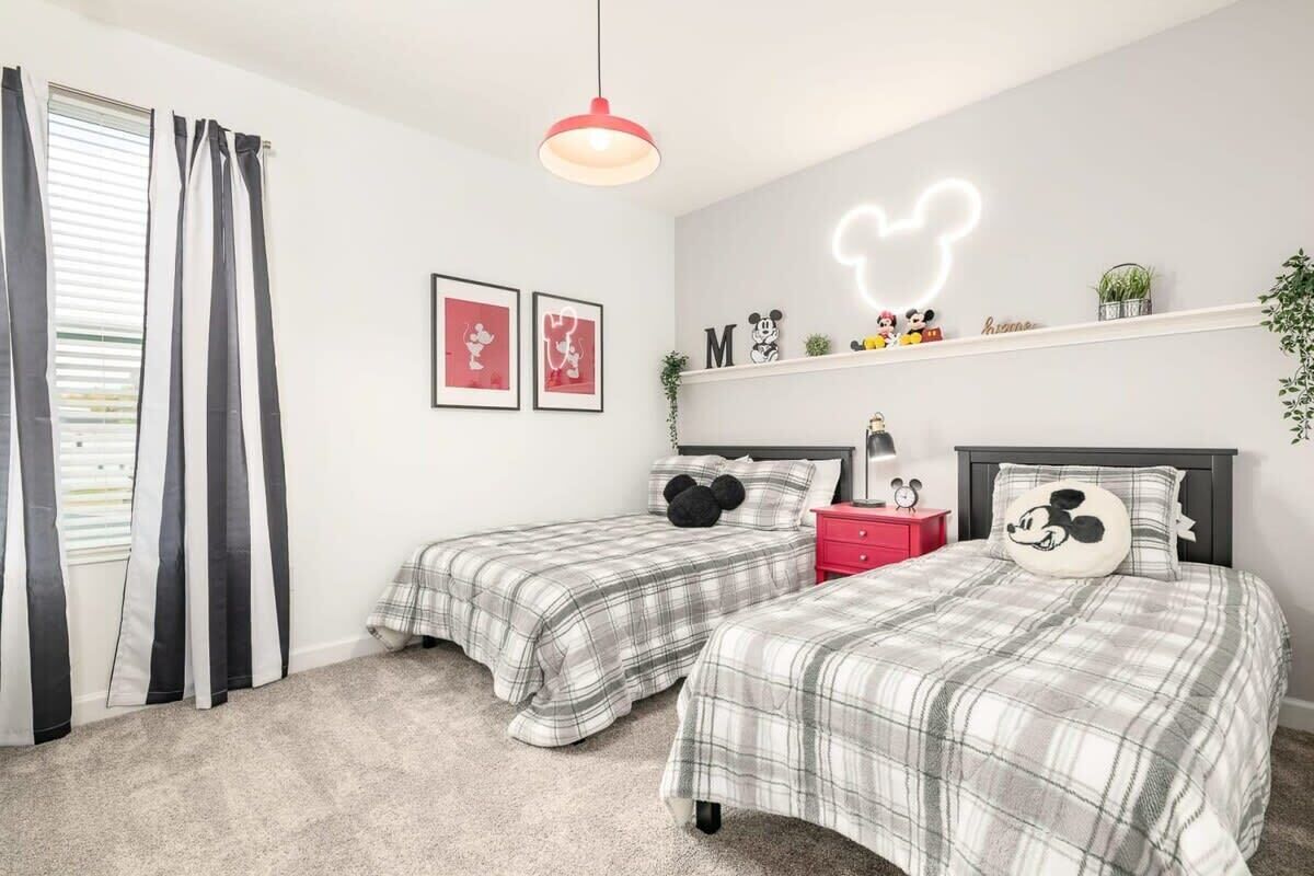 Ein Schlafzimmer mit zwei Betten, einem roten Nachttisch, einem Kissen mit Mickey Mouse Motiv und einem Neon-Schild mit Mickey Mouse an der Wand.