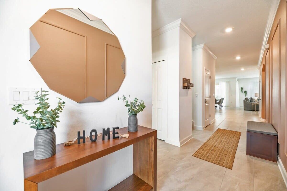 Un pasillo con una consola de madera, un espejo geométrico de pared y un letrero que dice 'HOME'.