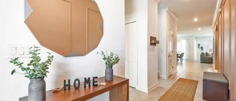 Un pasillo con una consola de madera, un espejo geométrico de pared y un letrero que dice 'HOME'.