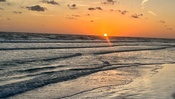 Un coucher de soleil sur l’océan, avec des vagues qui se brisent sur le rivage.