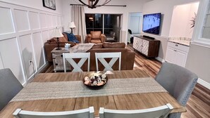 Un coin repas avec une table en bois, des chaises blanches et un lustre.