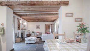 Una sala de estar acogedora con chimenea, un sofá, una mesa de comedor con mantel a cuadros y techo de madera.