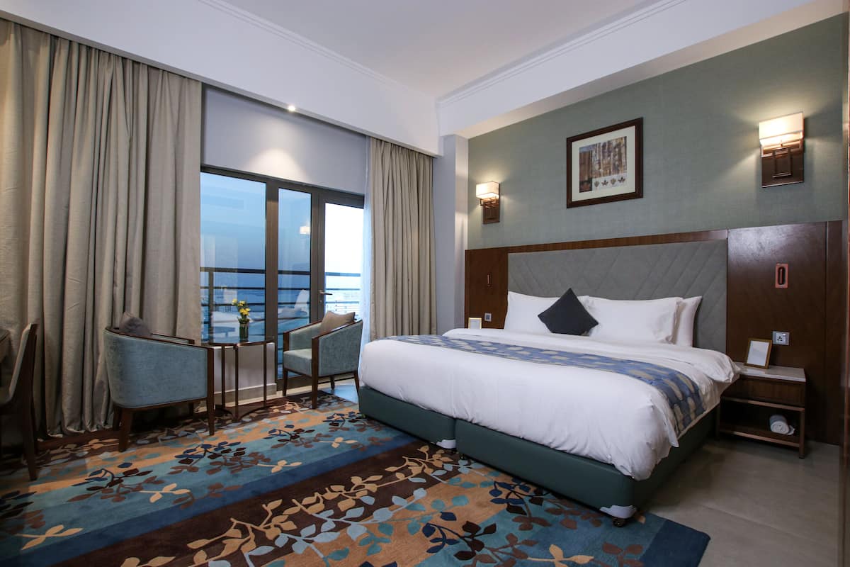 A hotel room with a large bed, a desk, a chair, and a view of the ocean.
