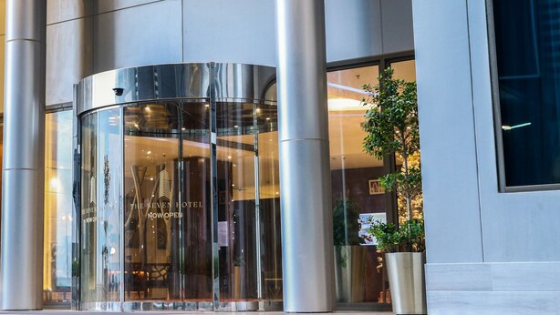 A modern hotel entrance with a revolving door and a large glass facade. - The Seven Hotel (Manama)