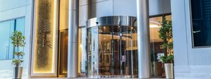 A modern hotel entrance with a revolving door and a large glass facade. - The Seven Hotel (Manama)