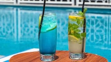 Dos vasos de bebidas con pajitas y adornos, sobre una superficie de madera junto a una piscina.