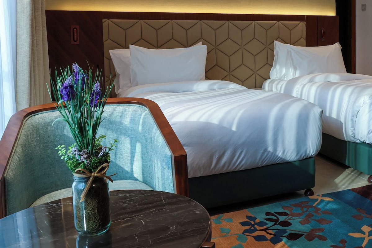A hotel room with two beds, a small table with a vase of flowers, and a patterned rug.