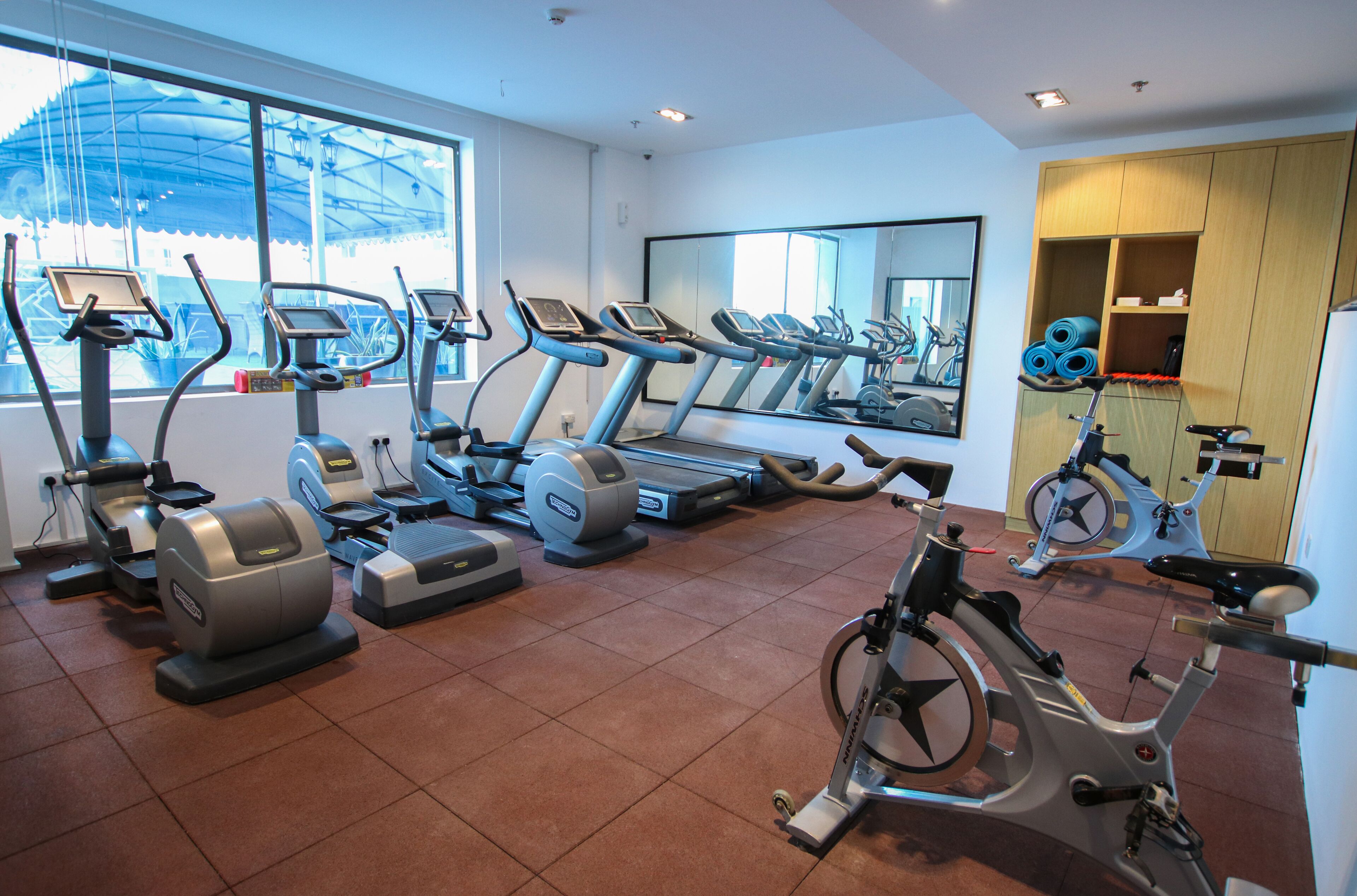 A gym with various exercise machines, a large mirror, and a view of the outside through large windows.