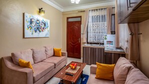 Sala de estar con sofá, mesa de centro, un cuadro, área de cocina y una puerta.