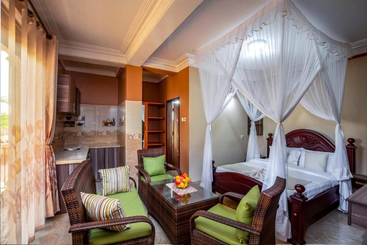 Une chambre d’hôtel comprenant un lit, un coin salon avec des fauteuils et une table, un coin cuisine et une salle de bain.