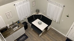 Cocina compacta con lavamanos, encimera y una pequeña zona de comedor con mesa y banco.