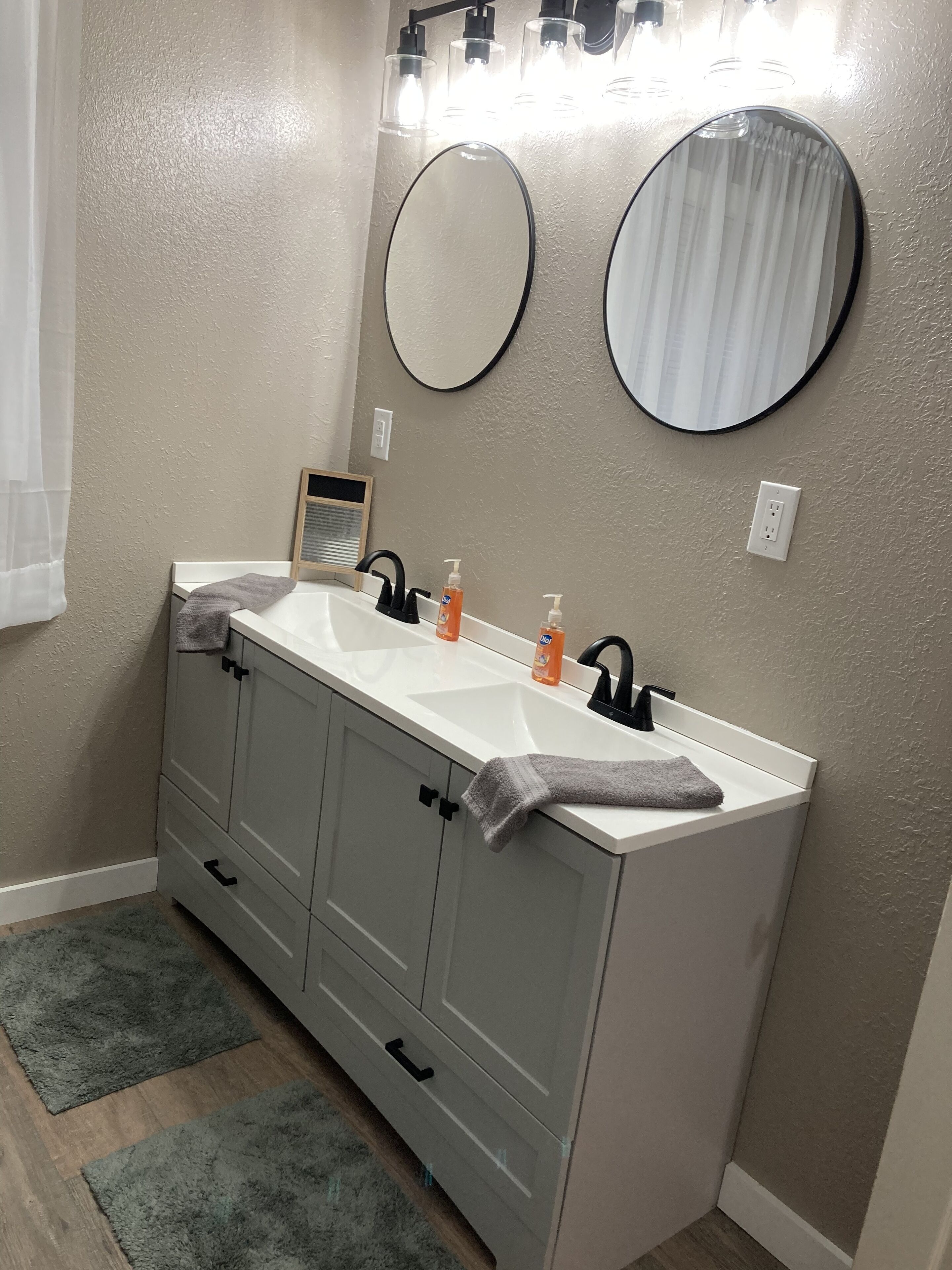 A bathroom with a double sink, two round mirrors, and a towel rack.
