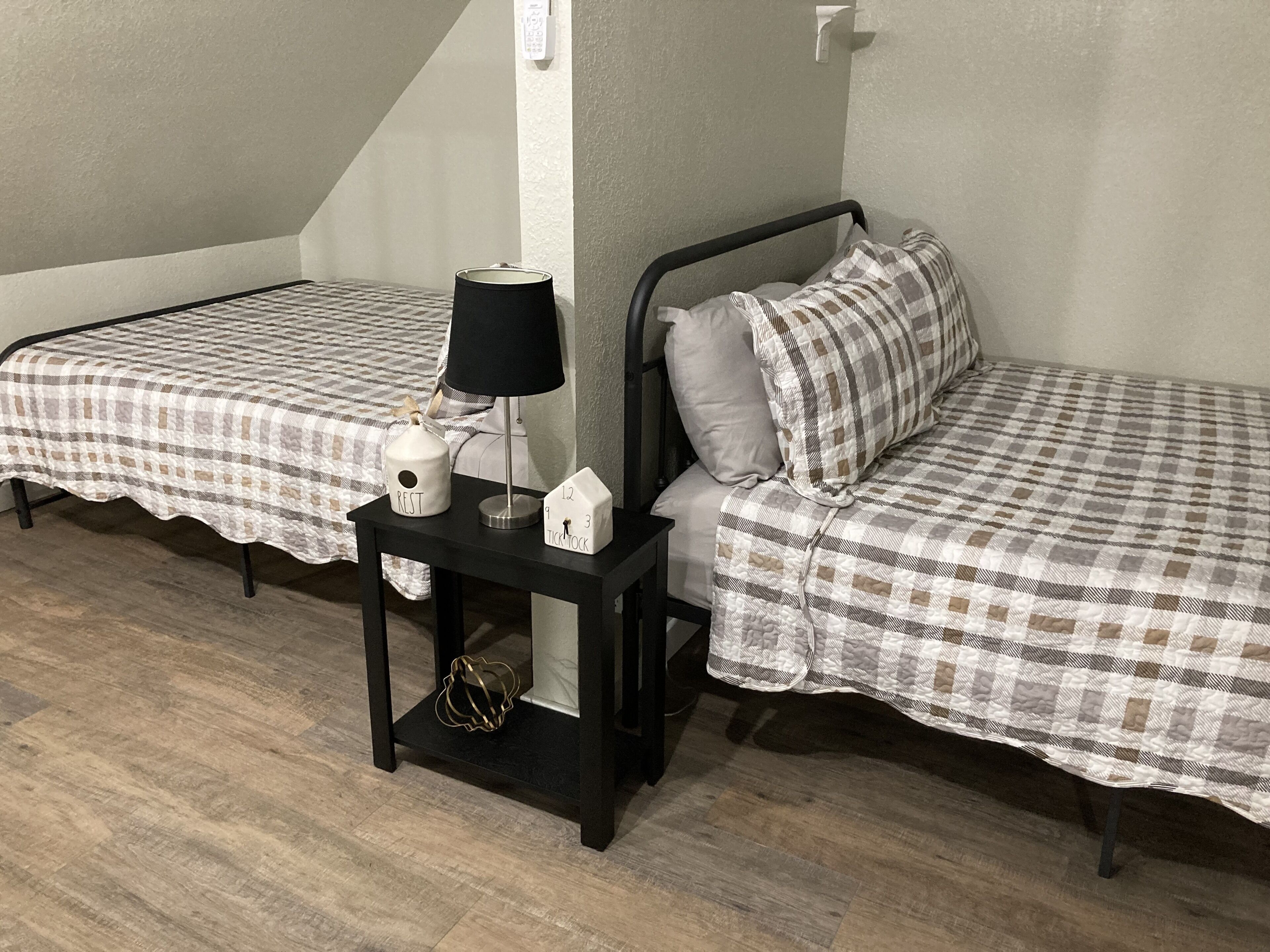Une chambre avec deux lits simples, une table de chevet avec une lampe, une horloge et un objet décoratif.