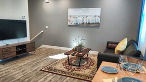 A modern living room with a flat-screen TV, a sofa, a dining table set with plates and glasses, and a decorative painting on the wall. - Flat at the Cork Oak · Sunny, central, quiet flat + yard (Petaluma)