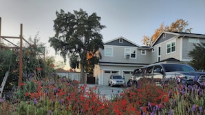 A residential house with a garage, two cars parked in front, and a garden with red and purple flowers. - Flat at the Cork Oak · Sunny, central, quiet flat + yard (Petaluma)