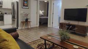 A modern living room with a sofa, coffee table, and TV. There is a kitchen area with a refrigerator and oven. - Flat at the Cork Oak · Sunny, central, quiet flat + yard (Petaluma)