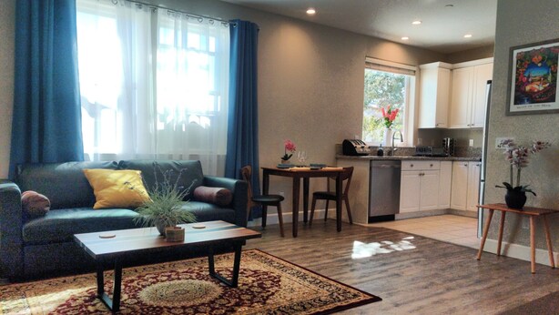 A living room with a sofa, coffee table, and rug. There is a kitchen area with a dining table and chairs. - Flat at the Cork Oak · Sunny, central, quiet flat + yard (Petaluma)
