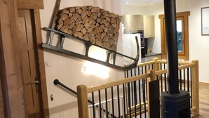 A wooden staircase with a black stove, a wall-mounted log rack, and a kitchen in the background.