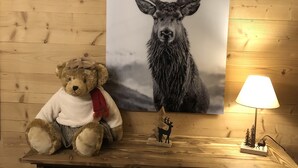 A wooden wall with a framed deer picture, a teddy bear, and a small lamp.