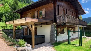 A wooden chalet with a balcony, stone walls, and a hot tub.