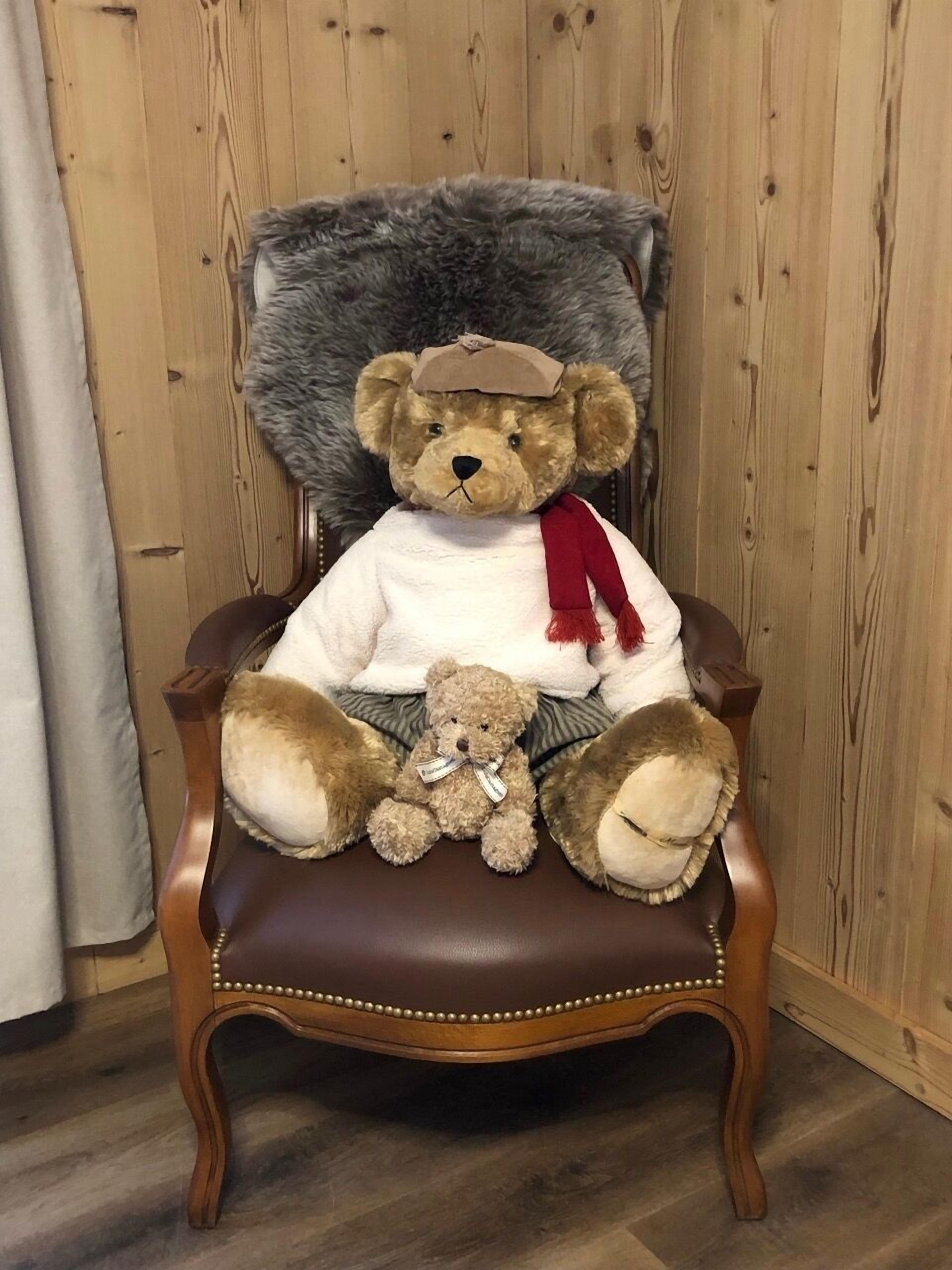 A plush teddy bear seated on a wooden chair with a fur backrest.